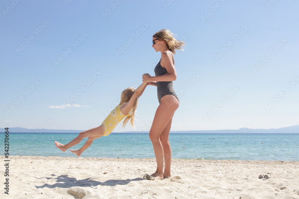 Mother and daughter having fun on the beach. Mother holding girls hands and spinning around. Family outdoor activities concept. Mother and daughter having fun on the beach. Mother holding girls hands and spinning around. Family outdoor activities concept.