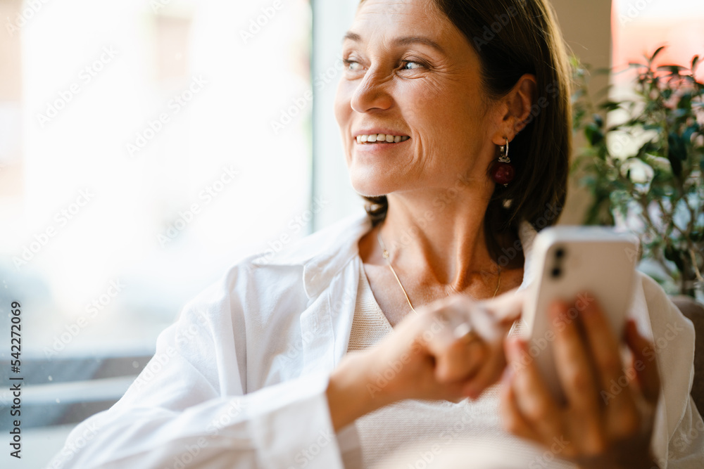 White mature woman using cellphone while sitting in cafe indoors White mature woman using cellphone while sitting in cafe indoors