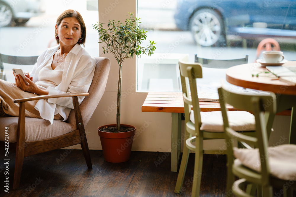 White mature woman using cellphone while sitting in cafe indoors White mature woman using cellphone while sitting in cafe indoors