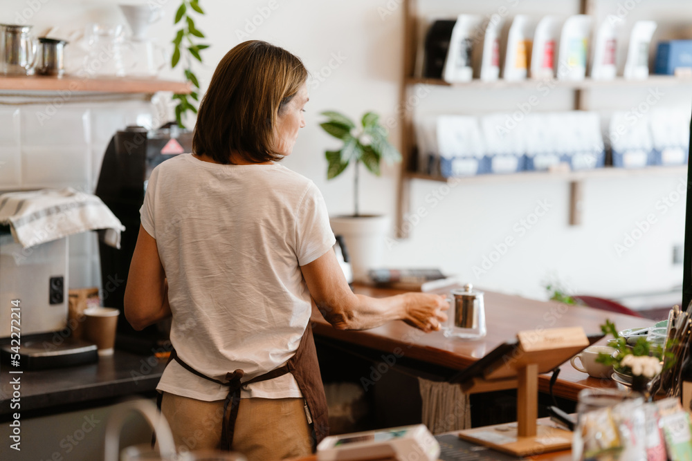 White mature barista woman making tea while working in cafe White mature barista woman making tea while working in cafe