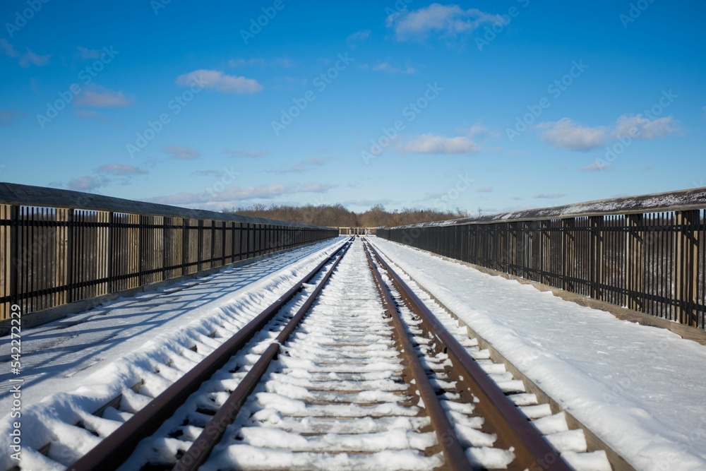 Empty railway track covered in snow under a blue cloudy sky on a sunny day