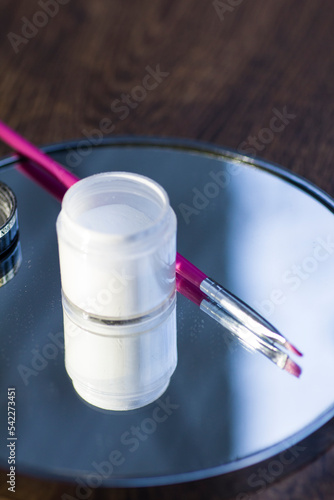 White acrylic powder to strengthen the nail plate and a brush in the reflection of the mirror