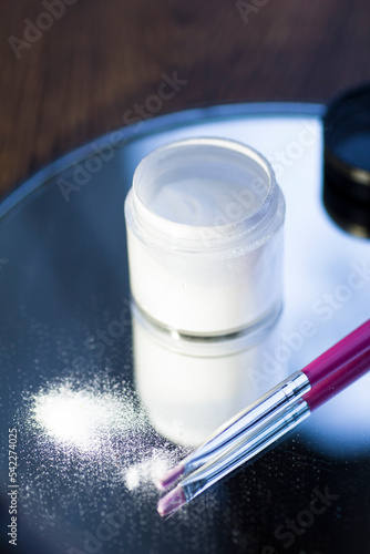 White acrylic powder to strengthen the nail plate and a brush in the reflection of the mirror