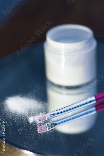 White acrylic powder to strengthen the nail plate and a brush in the reflection of the mirror