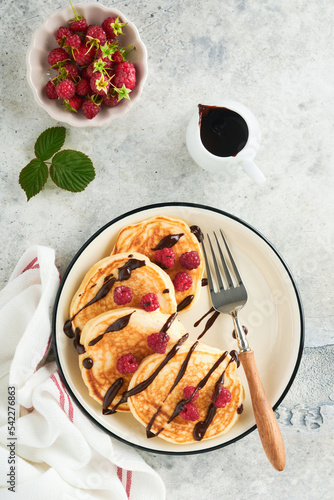 American pancakes. Pancakes with fresh raspberry with chocolate glaze or toppings in gray bowl on light gray table background. Homemade classic american pancakes. Page for magazine concept. Top view.