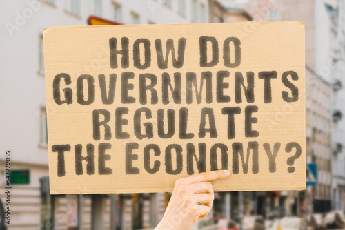 The question " How do governments regulate the economy? " is on a banner in men's hands with blurred background. Pay. Public. Return. Rule. Subsidy. Advice. Assistance. Balance. Coin. Exchange. Debt