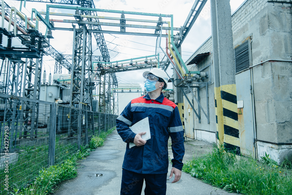 A masked power engineer during a pandemic inspects the modern equipment of an electrical substation before commissioning. Energy and industry. Scheduled repair of electrical equipment. A masked power engineer during a pandemic inspects the modern equipment of an electrical substation before commissioning. Energy and industry. Scheduled repair of electrical equipment.