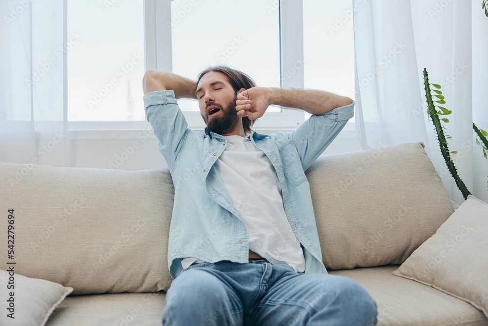 A man sits on the couch yawning and stretching after a nap, lack of sleep and fatigue from work and improper daily routine.