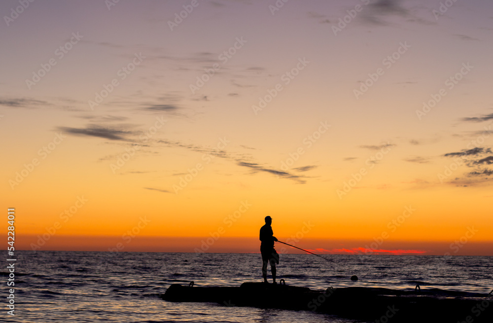 Fototapeta premium silhouette of man on pier by sea against sunset. male fisherman holds fishing rod, beautiful seascape. lonely man.