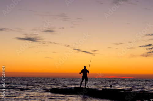 silhouette of  man on  pier by  sea against  sunset.  male fisherman holds  fishing rod,  beautiful seascape.  lonely man.