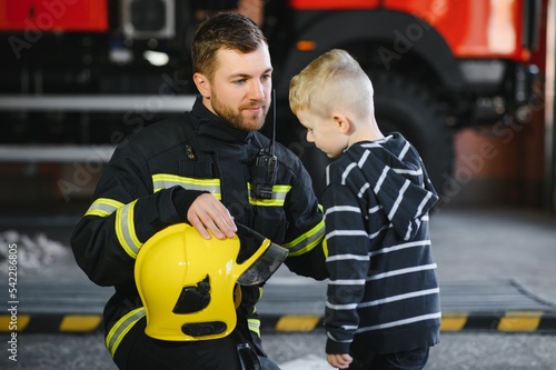A firefighter take a little child boy to save him. Fire engine car on background. Fireman with kid in his arms. Protection concept.