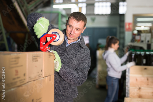 Man sealing carton boxes with sticky tape dispenser at warehouse on artisanal olive oil factory photo