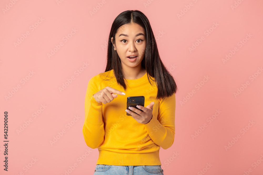 Surprised woman holding mobile phone standing on pink background. Good news, discounts or sale, online shopping concept Surprised woman holding mobile phone standing on pink background. Good news, discounts or sale, online shopping concept