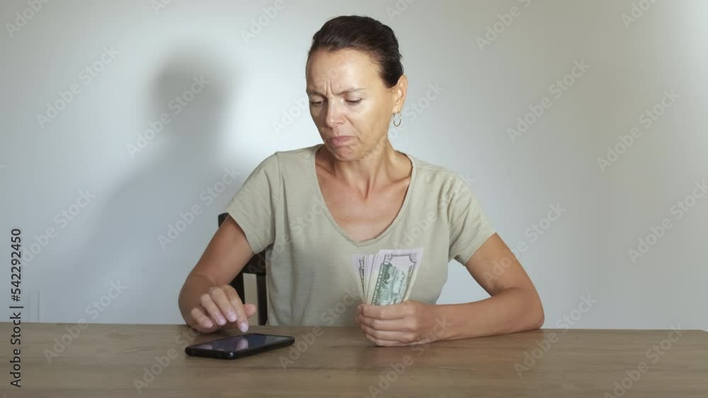 Pensive woman with last money. A pensive woman count her budget on her smartphone and hold her last dollars in her hand. A concept of household financial problems and world economical inflation. Pensive woman with last money. A pensive woman count her budget on her smartphone and hold her last dollars in her hand. A concept of household financial problems and world economical inflation.