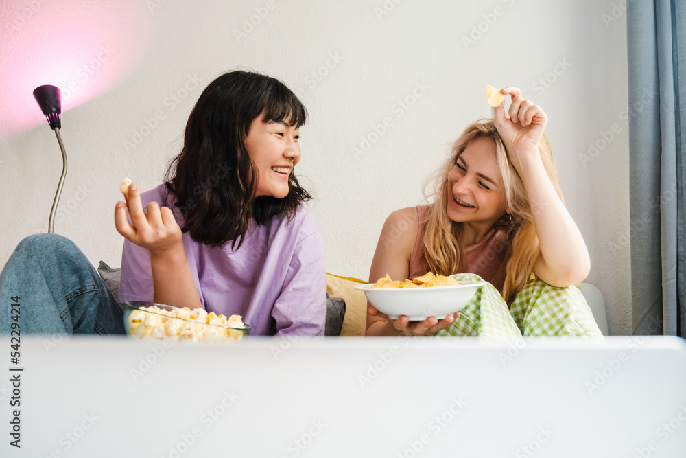 Two multiracial girls eating snacks while watching movie together Two multiracial girls eating snacks while watching movie together