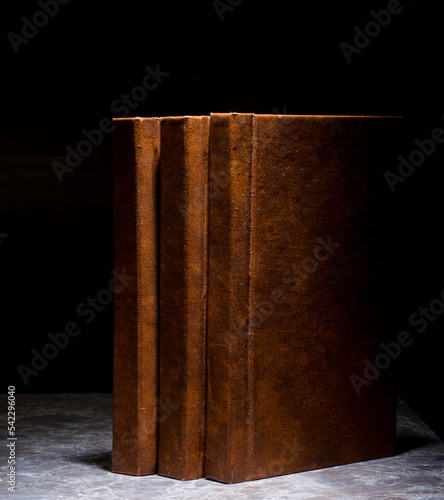 several books with the same binding on a dark background isolated. three books with a brown cover without inscriptions and titles with free space for text photo