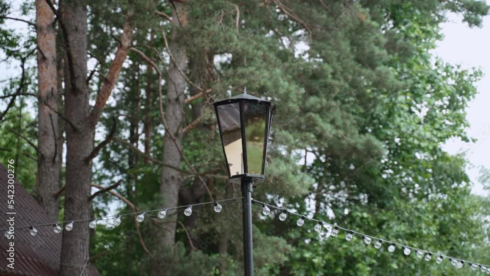 Old iron black retro lantern with mirrored glasses stands near green trees. Old iron black retro lantern with mirrored glasses stands near green trees.