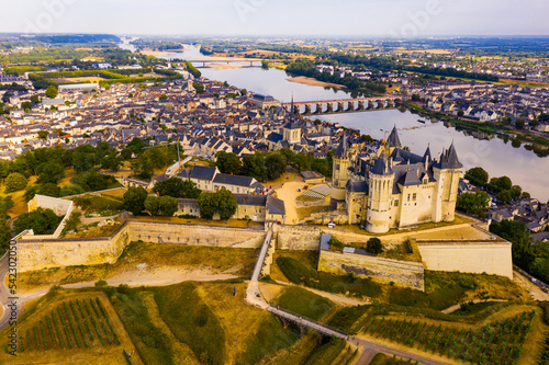 Fototapeta Naklejka Na Ścianę i Meble -  Scenic aerial view of Saumur town overlooking ancient fortified Chateau with Cessart arched bridge over Loire river in background in summer, France