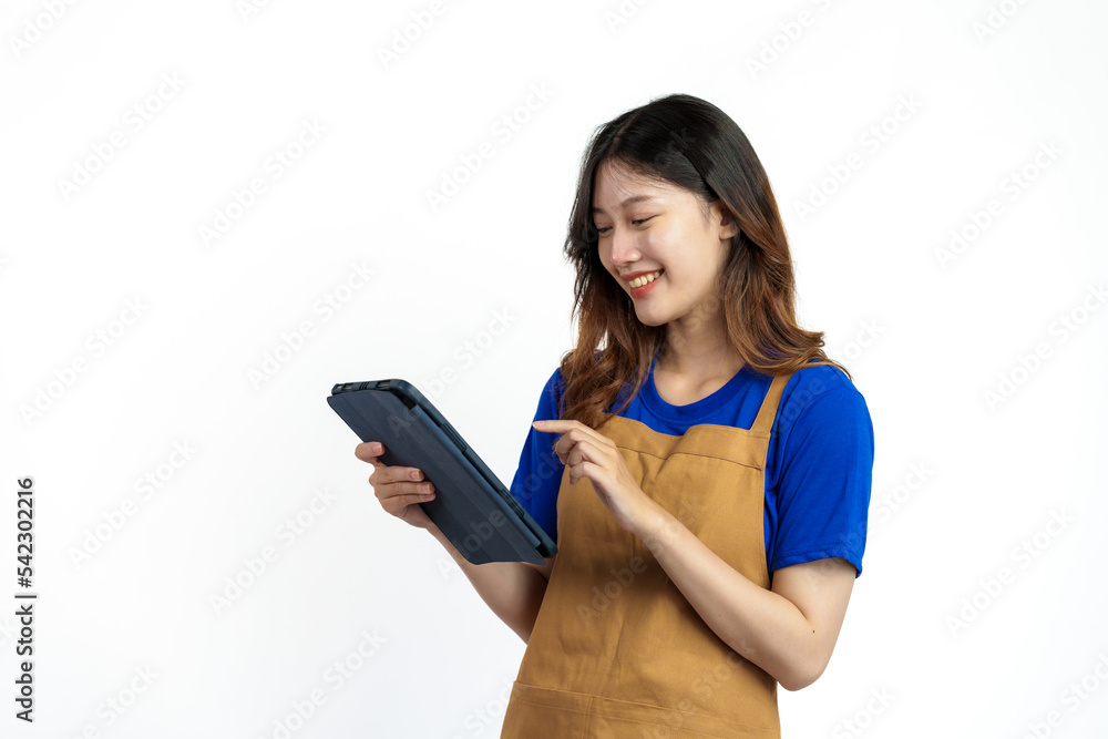 Using tablet, Cheerful young pretty asian woman blue t-shirt and apron coffee owner isolated on white background. checking order online Using tablet, Cheerful young pretty asian woman blue t-shirt and apron coffee owner isolated on white background. checking order online