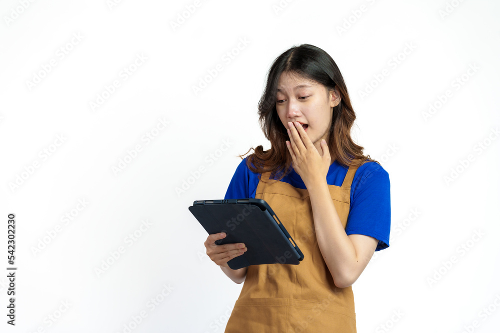 Using tablet, Cheerful young pretty asian woman blue t-shirt and apron coffee owner isolated on white background. checking order online Using tablet, Cheerful young pretty asian woman blue t-shirt and apron coffee owner isolated on white background. checking order online