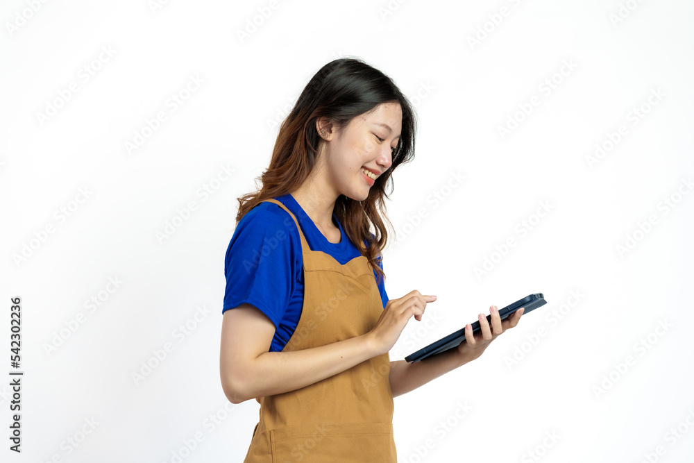 Using tablet, Cheerful young pretty asian woman blue t-shirt and apron coffee owner isolated on white background. checking order online Using tablet, Cheerful young pretty asian woman blue t-shirt and apron coffee owner isolated on white background. checking order online