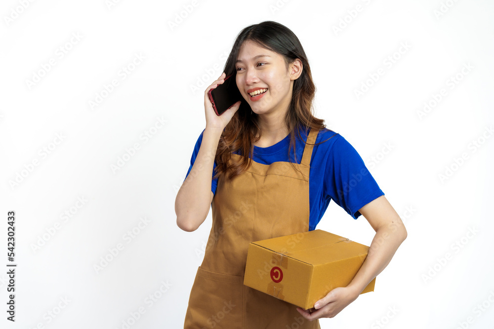 Young pretty asian woman with apron holding packages box of product for delivery sme entrepreneur owner isolated on white background. Using mobile Young pretty asian woman with apron holding packages box of product for delivery sme entrepreneur owner isolated on white background. Using mobile