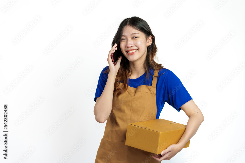 Young pretty asian woman with apron holding packages box of product for delivery sme entrepreneur owner isolated on white background. Using mobile Young pretty asian woman with apron holding packages box of product for delivery sme entrepreneur owner isolated on white background. Using mobile