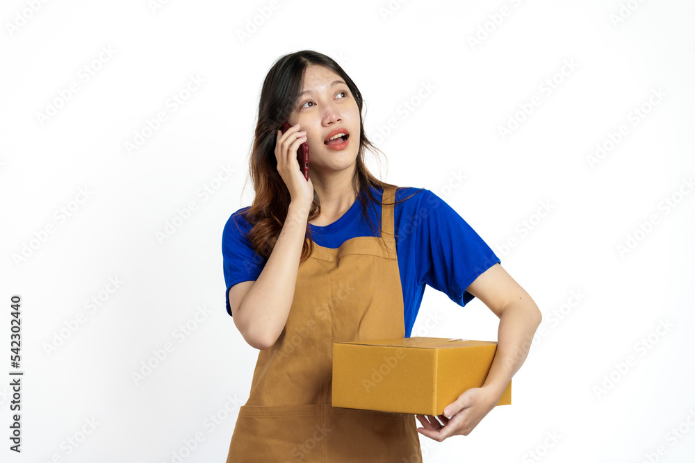 Young pretty asian woman with apron holding packages box of product for delivery sme entrepreneur owner isolated on white background. Using mobile Young pretty asian woman with apron holding packages box of product for delivery sme entrepreneur owner isolated on white background. Using mobile