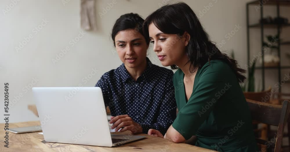 Two multi ethnic women colleagues staring at laptop screen, learn new task or discuss corporate software, prepare presentation, search solution, mentor explaining program. Workflow use tech, teamwork Two multi ethnic women colleagues staring at laptop screen, learn new task or discuss corporate software, prepare presentation, search solution, mentor explaining program. Workflow use tech, teamwork