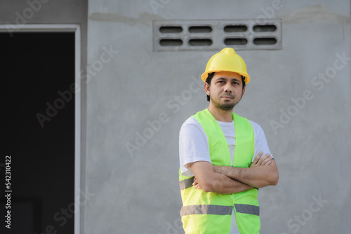 portrait of asian male construction worker standing with his arms crossed at construction site with copy space