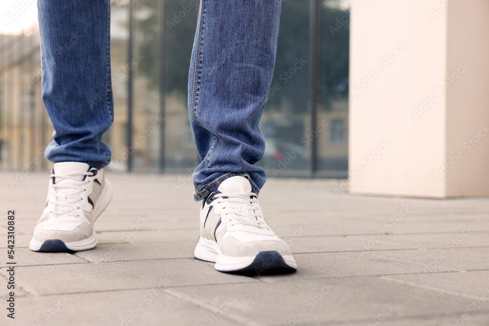 Man in jeans and sneakers walking on city street, closeup. Space for text Man in jeans and sneakers walking on city street, closeup. Space for text