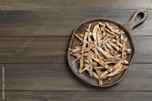 Serving board with tasty dried anchovies on wooden table, top view. Space for text