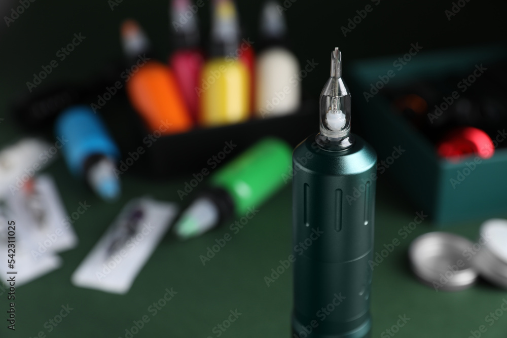 Naklejka premium Tattoo machine and tools on dark green table, closeup