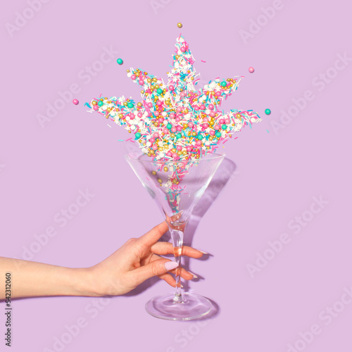 Martini glass with colorfool glitter and a woman's hand on pastel purple backgraund . Party drink concept art. Minimal New Year surrealism. photo