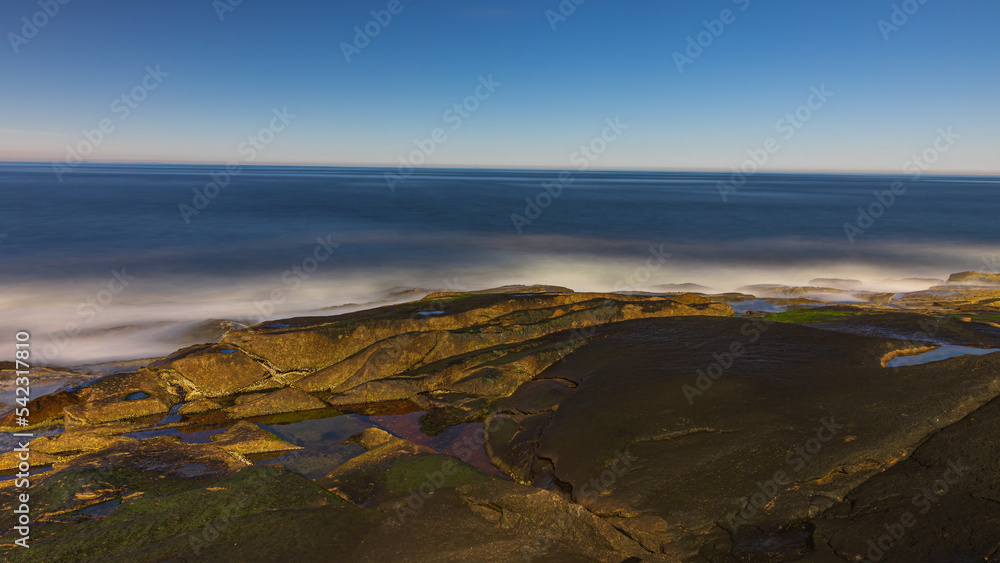 Misty Water In Rocky Beach Landscape. Sunrise At the Atlantic Ocean. Large Rocks Merge Into Misty Ocean. Ocean Merges With The Blue Sky In Horizon. Misty Water In Rocky Beach Landscape. Sunrise At the Atlantic Ocean. Large Rocks Merge Into Misty Ocean. Ocean Merges With The Blue Sky In Horizon.