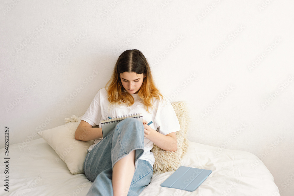 A teenage girl is drawing or doing homework in the bedroom. A teenager studies at home. Back to school A teenage girl is drawing or doing homework in the bedroom. A teenager studies at home. Back to school