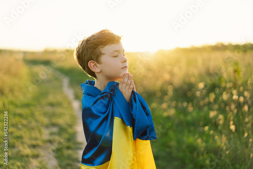 Ukrainian boy closed her eyes and praying to stop the war in Ukraine in a field at sunset. Hands folded in prayer concept for faith, spirituality and religion. War of Russia against Ukraine. Stop War photo