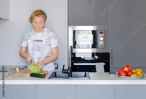 A woman cooking vegetarian food in a modern kitchen in gray tones. Blurry motion photo