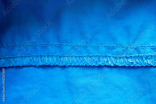 Overlock seam on blue fabric. Textured cloth background. Place for text. Flatley.  photo