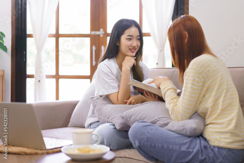 Relax at home concept, LGBT lesbian female is reading holy bible to girlfriend in living room