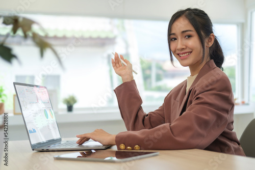 Confident businesswoman in stylish suit sitting front of laptop at her working desk and smiling to camera.