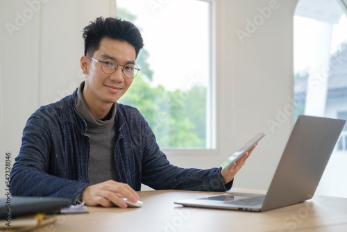 Smiling young man freelancer in stylish outfits using laptop computer in bright office.