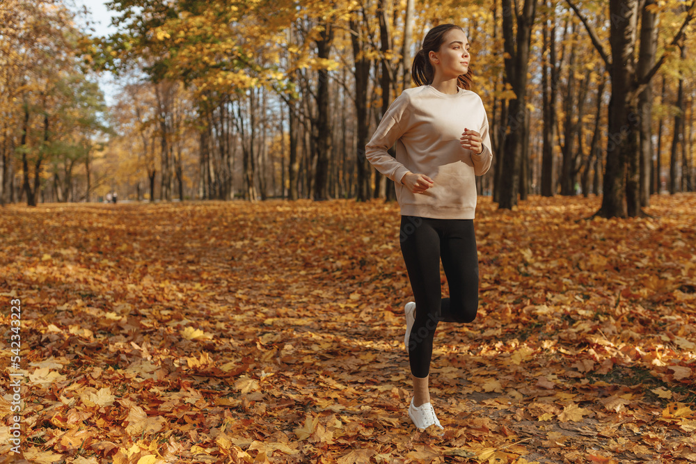 Full length of sporty woman running on path in autumn park during training on sunny day Full length of sporty woman running on path in autumn park during training on sunny day