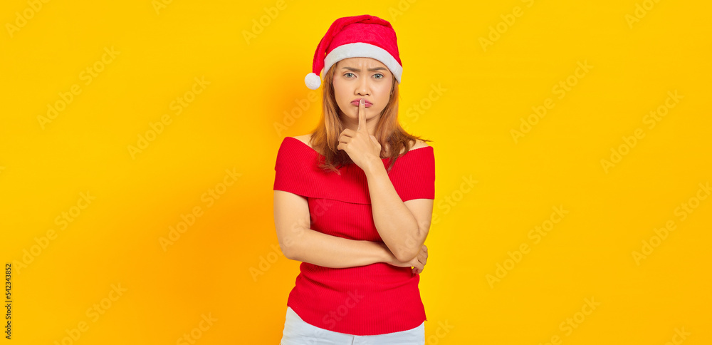 Attractive young Asian woman wearing christmas hat and making silence gesture on yellow background Attractive young Asian woman wearing christmas hat and making silence gesture on yellow background