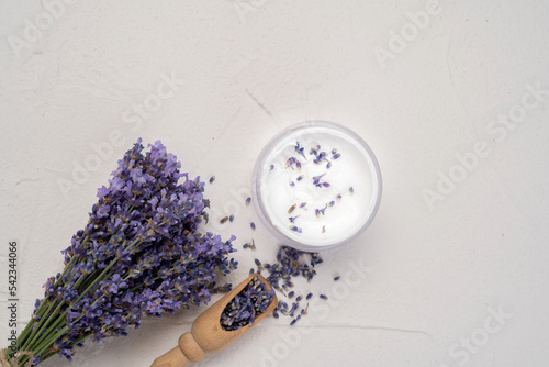 Bunch of fresh lavender flowers and moisturizing face cream on white background. Top view, flat lay mock up, copy space. Natural herbal cosmetics. Minimal background
