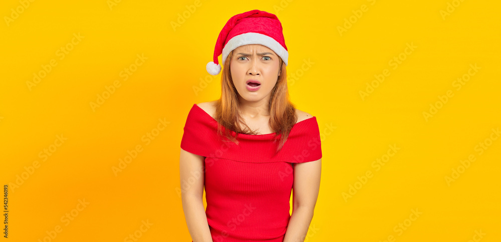 Portrait of surprised young Asian woman with open mouth and wearing Christmas hat on yellow background Portrait of surprised young Asian woman with open mouth and wearing Christmas hat on yellow background