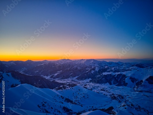Vertical aerial panorama of snowy mountain ridge on winter sunrise. Stunning mountains range covered with snow at sunset afterglow. Caucasus mountain peaks skyline in the twilight golden hour. © artiemedvedev