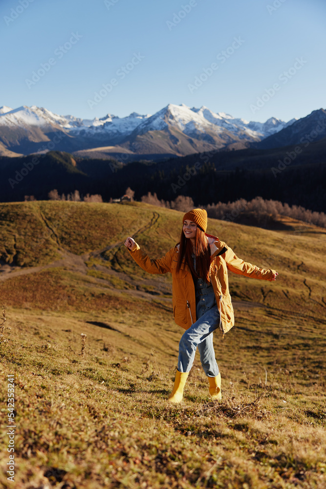 Full-length woman running up the hill to the camera and looking out at the mountains in a yellow raincoat and jeans in the autumn happy sunset camping trip, freedom lifestyle Full-length woman running up the hill to the camera and looking out at the mountains in a yellow raincoat and jeans in the autumn happy sunset camping trip, freedom lifestyle