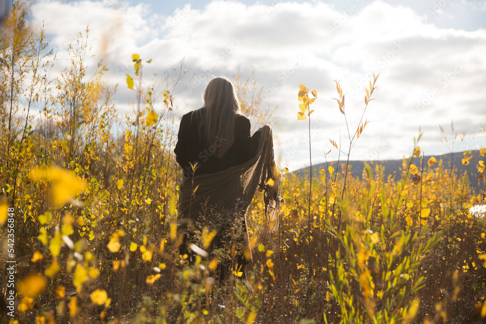 Fototapeta premium elderly woman with gray hair wearing a brown coat stands with his back on the bank of the river. Slow life. Enjoying the little things. nature walks. greyhairdontcare