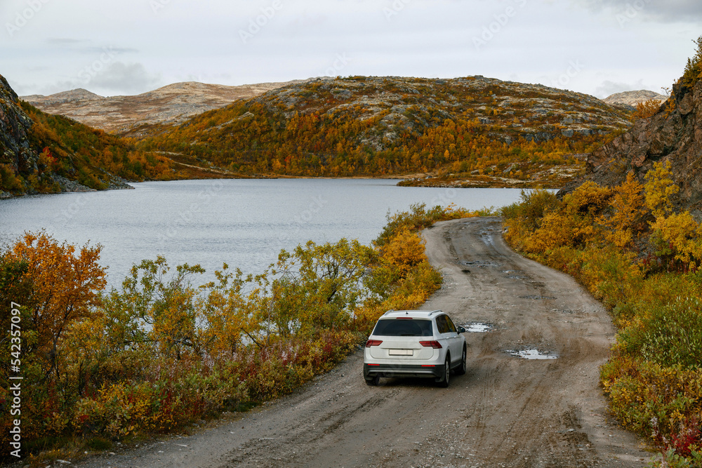 Fototapeta premium A white car drives along a beautiful dirt road along northern landscapes